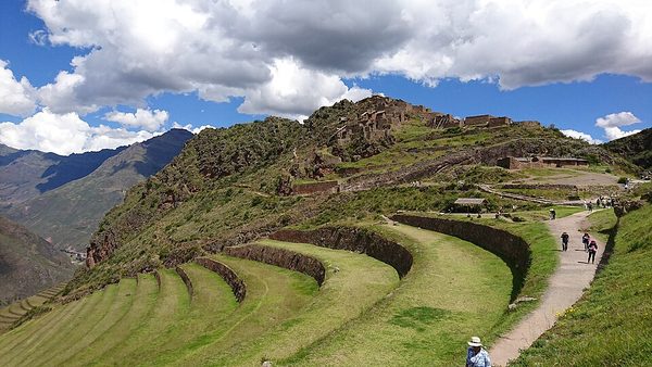 Curved stone-walled terraces stepping down a steep green mountainside below a hilltop ruin