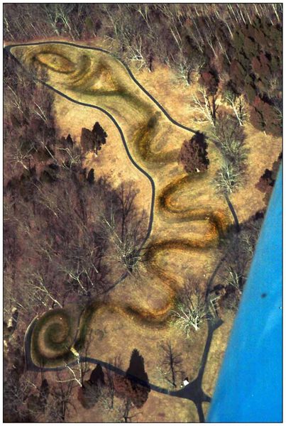 An aerial view of a long coiling snake-shaped earthen mound running across a mown clearing