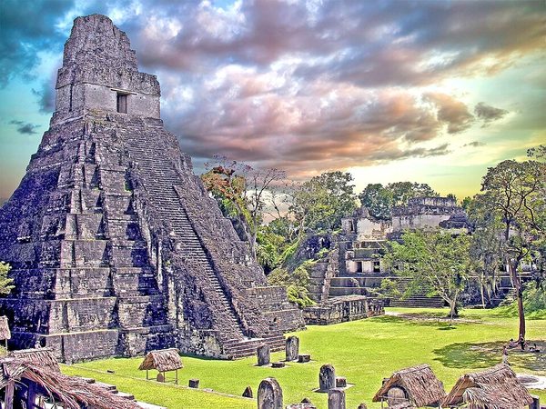 A tall steep stone pyramid with a temple and a high roof comb on top, above a grass plaza