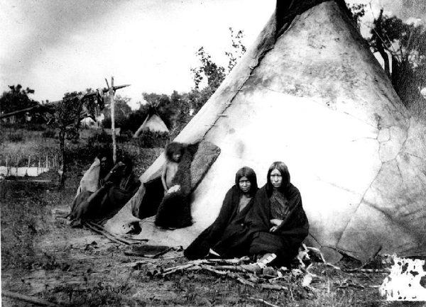 A large hide tepee with people seated in front of it