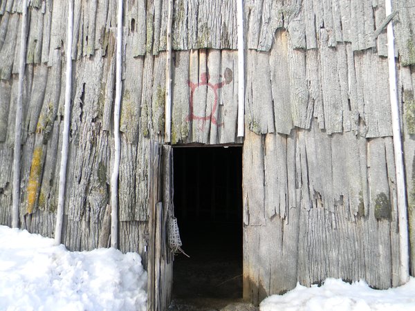 A longhouse walled in bark slabs, with a turtle painted in red above its open doorway