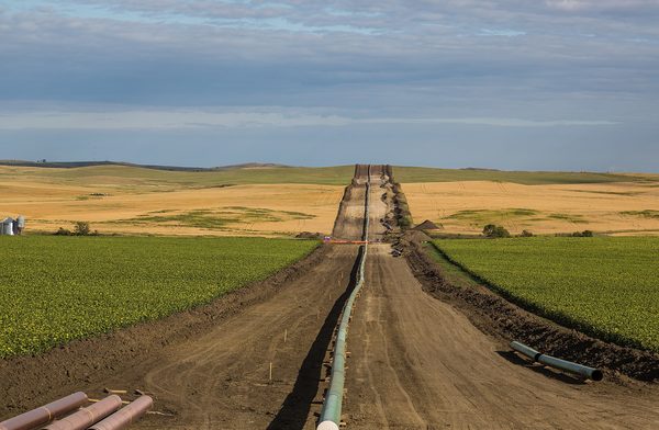 A pipeline being laid in a long trench cut straight through farmland
