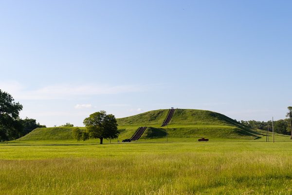 A wide flat-topped earthen mound with a staircase up its front, in open grassland